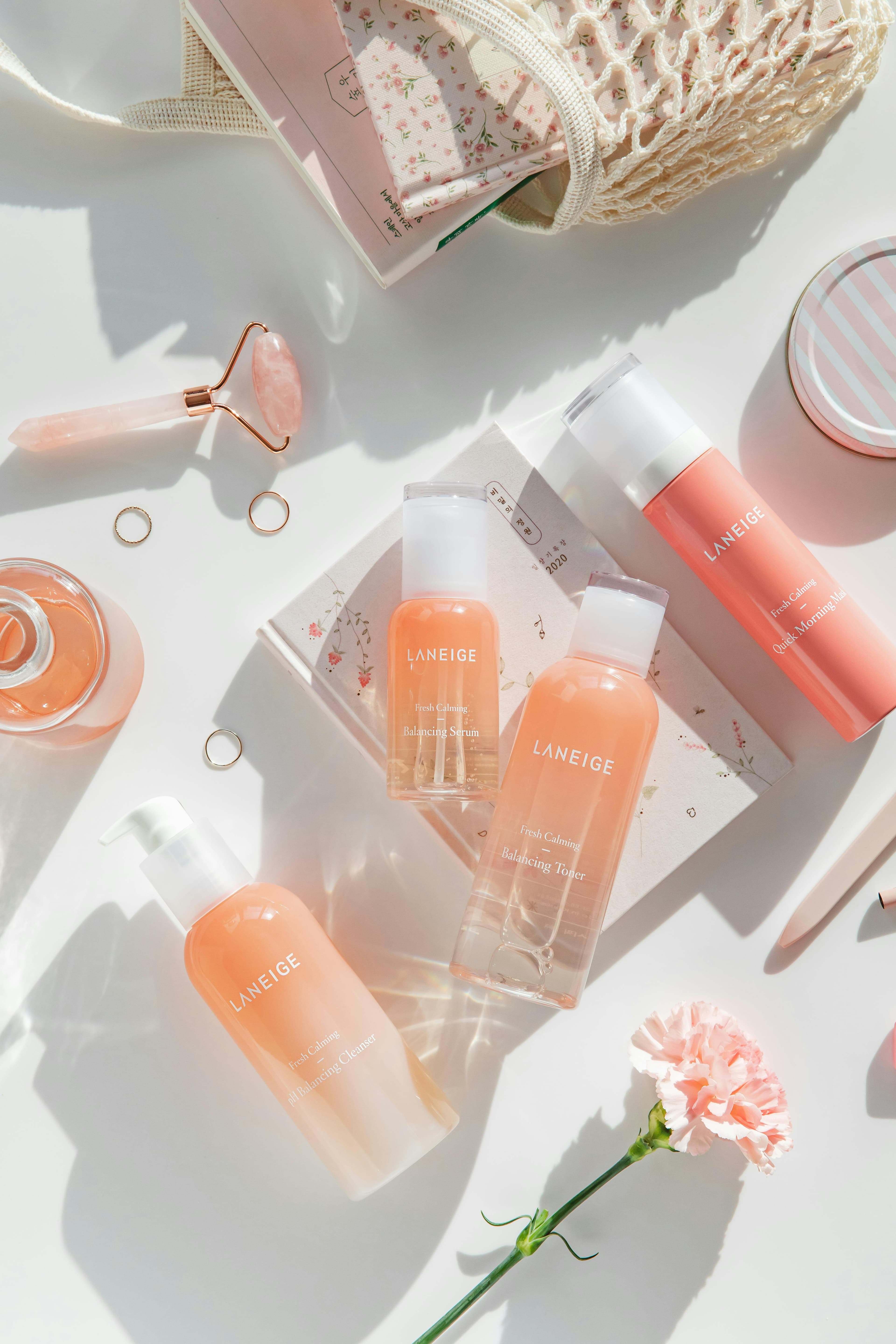 Soft pink flat lay of Korean skincare bottles and beauty accessories on a bright white surface.