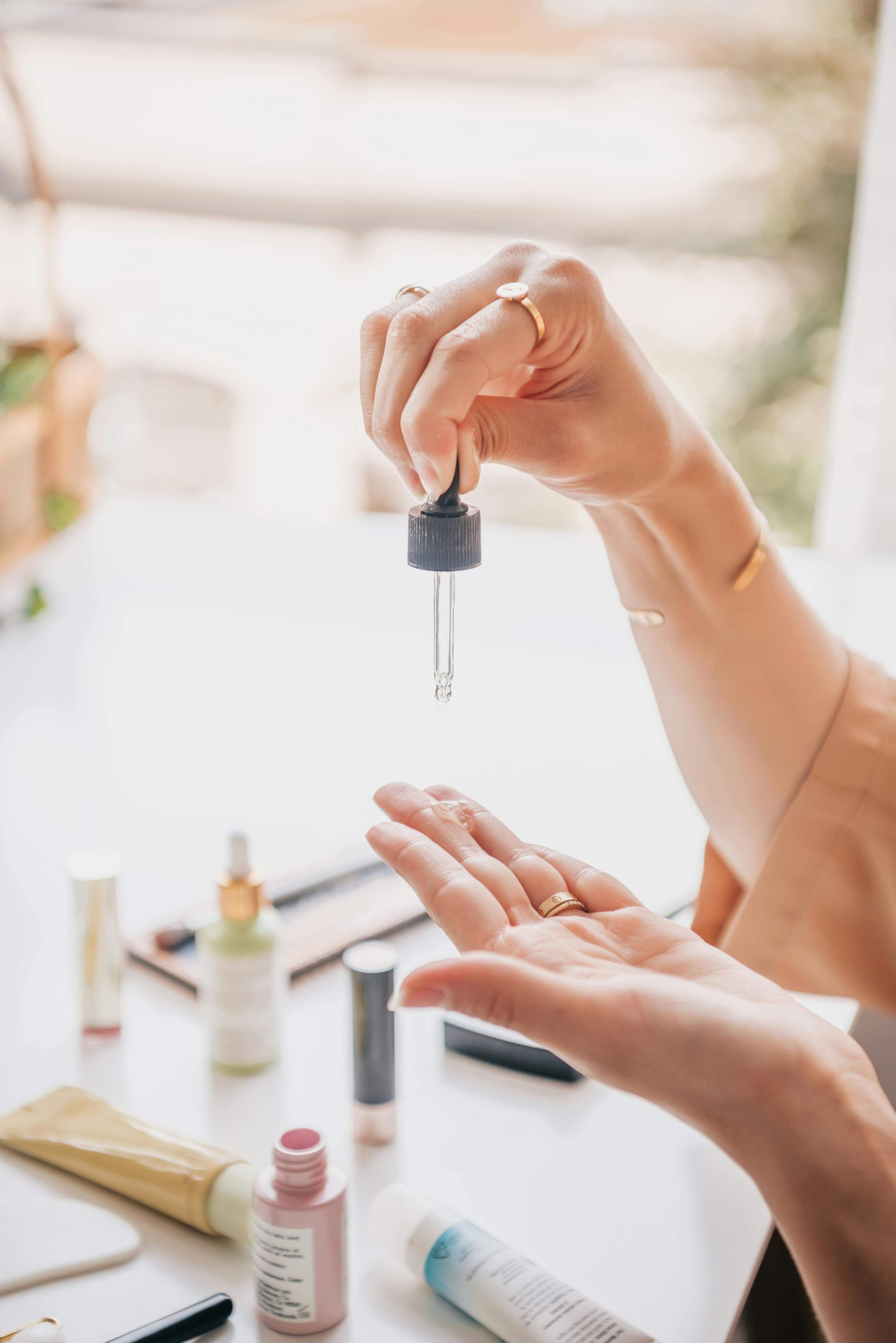 Hands applying a skincare serum with a dropper in soft morning light.